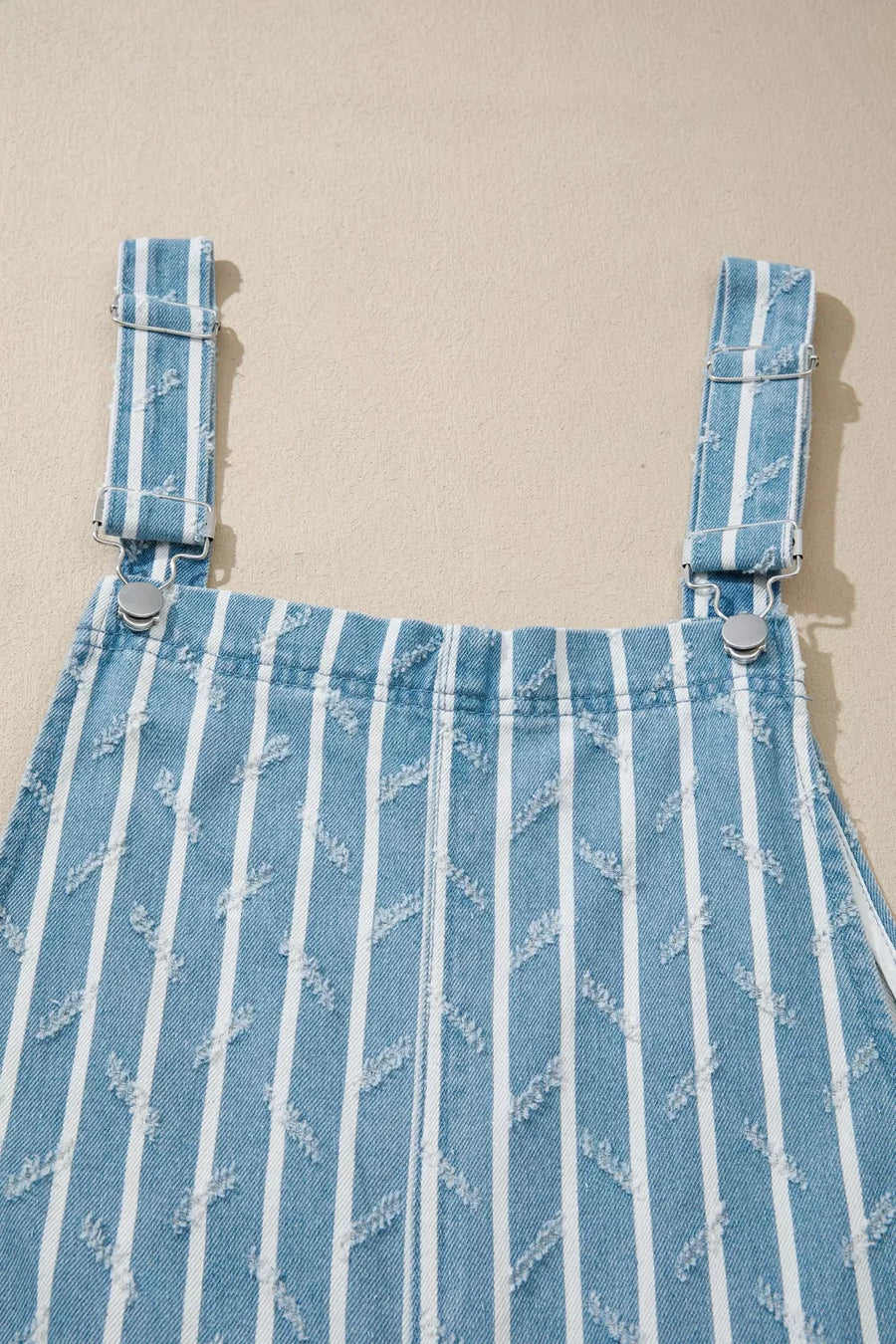 Striped distressed denim overalls with adjustable straps and metal hardware.