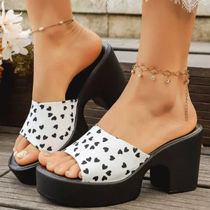 White and black heart print block heel slide sandals with platform sole.