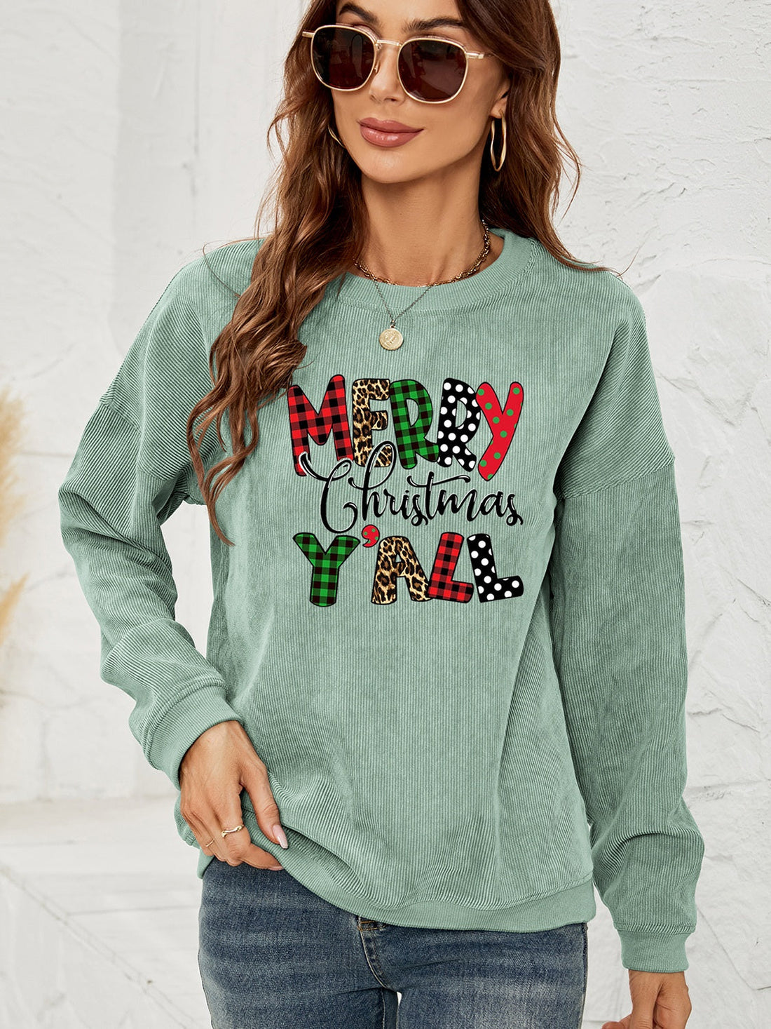 Sage corduroy sweatshirt with Merry Christmas Y'all graphic in buffalo plaid, leopard, and polka dot patterns.