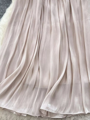 Cream pleated maxi skirt with flowing fabric and subtle sheen.