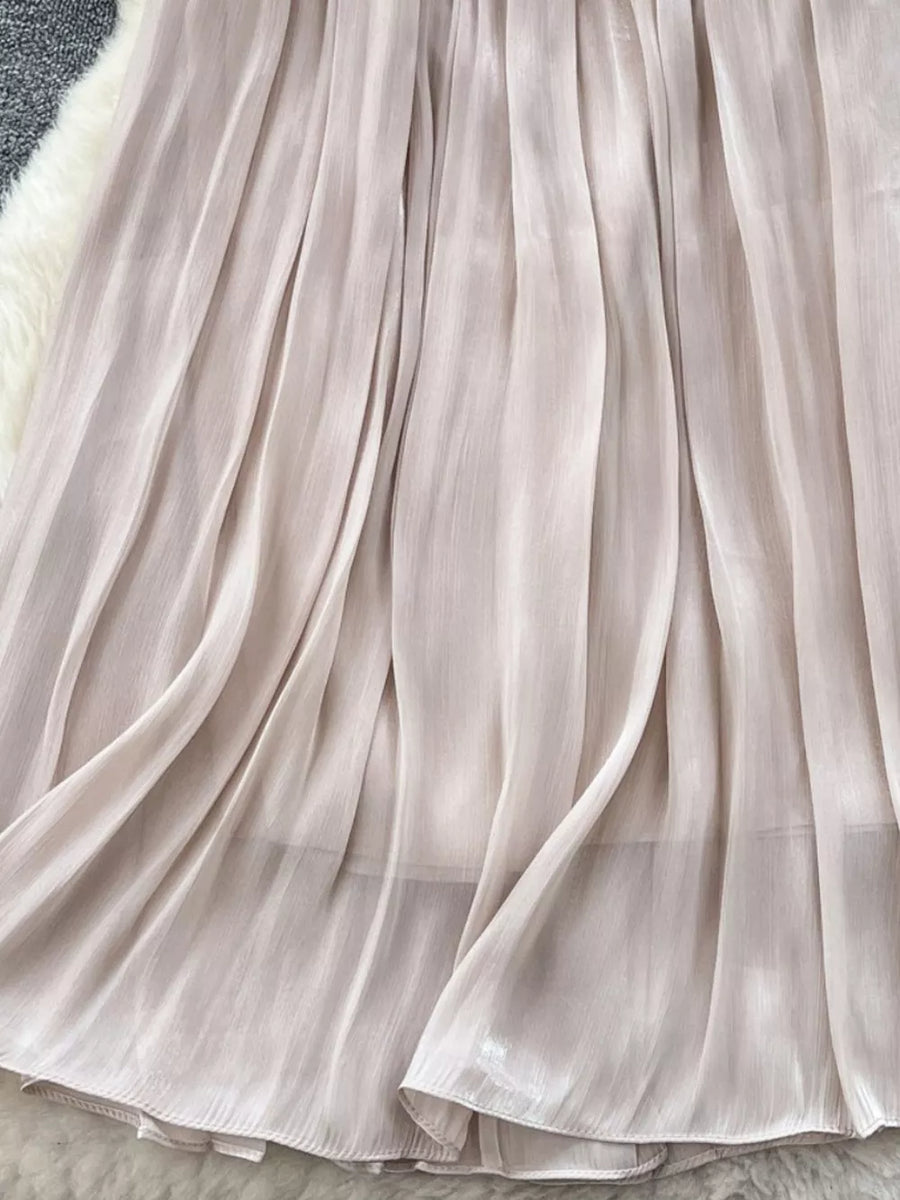 Cream pleated maxi skirt with flowing fabric and subtle sheen.
