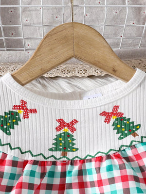 White baby dress with Christmas trees and red, green, and blue plaid skirt.