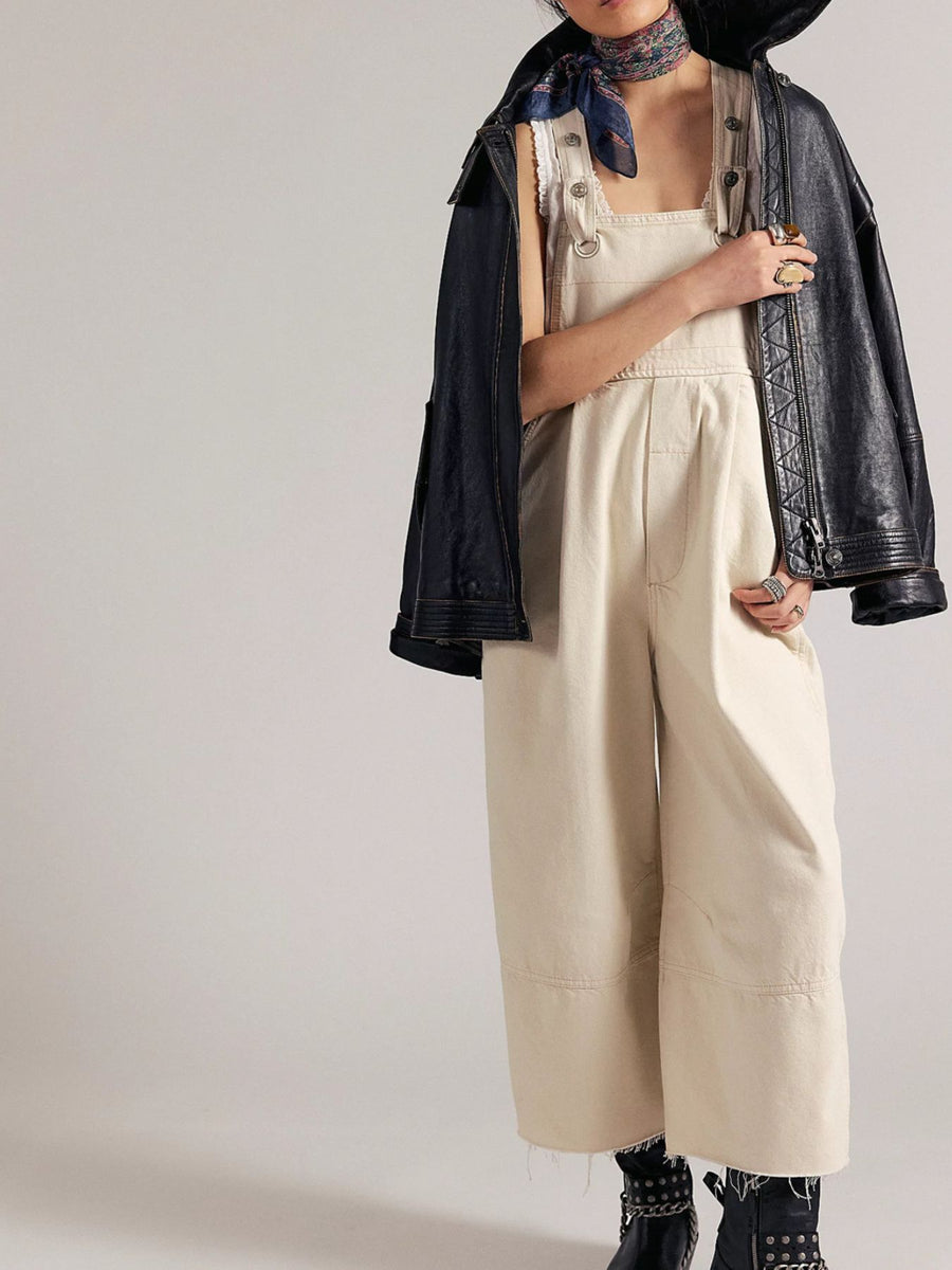 Beige wide-leg denim overalls with raw hem and adjustable straps, styled with a jacket.