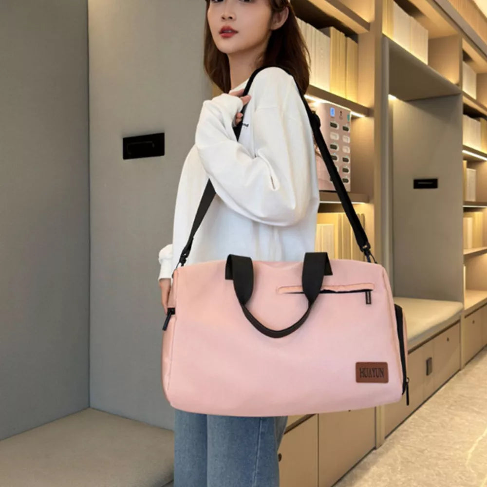 Pink nylon travel duffel bag with black straps and zipper pockets, worn by a woman.