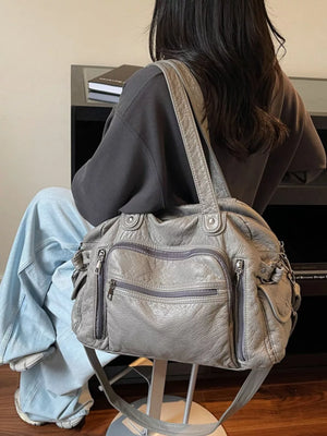 Gray leather hobo bag with multiple zippered pockets and a slouchy silhouette.