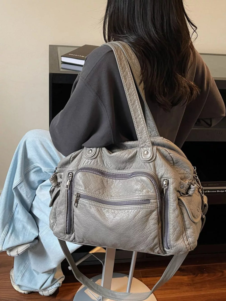 Gray leather hobo bag with multiple zippered pockets and a slouchy silhouette.