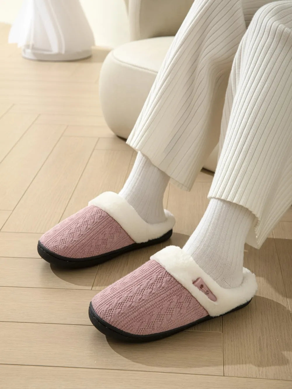 Dusty pink cable knit house slippers with shearling lining and a decorative button detail.