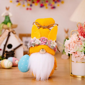Easter gnome with yellow bunny ears hat, floral crown, white beard, holding blue egg.