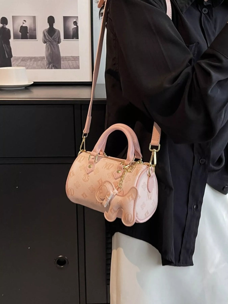 Pink mini barrel crossbody bag with embossed pattern and elephant charm.