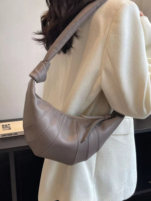 Grey hobo bag with curved stitching and knotted strap detail, worn crossbody.