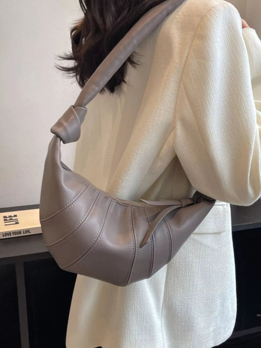 Grey hobo bag with curved stitching and knotted strap detail, worn crossbody.