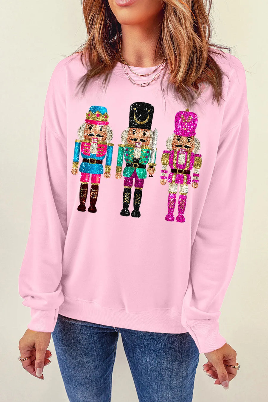 Blush pink crewneck sweatshirt with a graphic of three sequined nutcrackers.