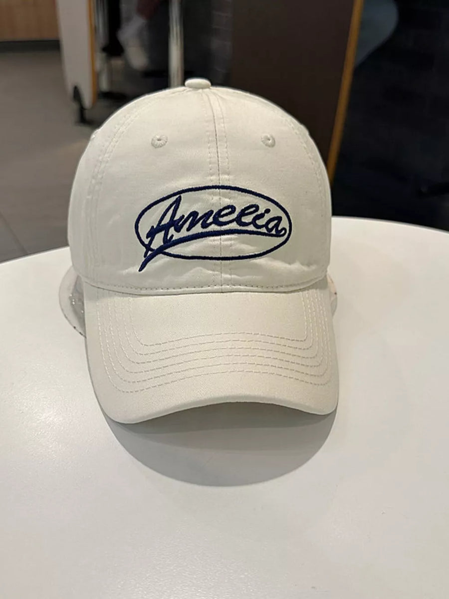 White baseball cap with navy blue Amelia embroidery and curved brim