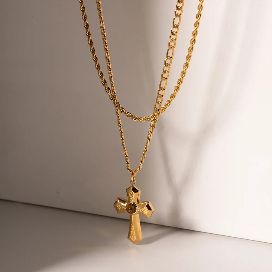 Gold layered chain necklace with a sculpted cross pendant featuring a central stone.