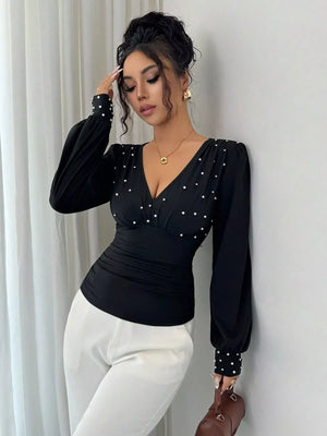 Black ruched V-neck blouse with pearl embellishments and long puff sleeves.