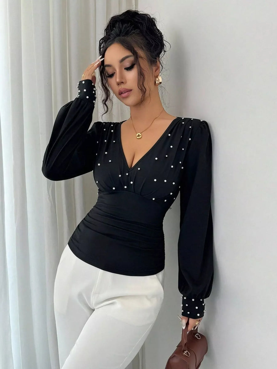 Black ruched V-neck blouse with pearl embellishments and long puff sleeves.