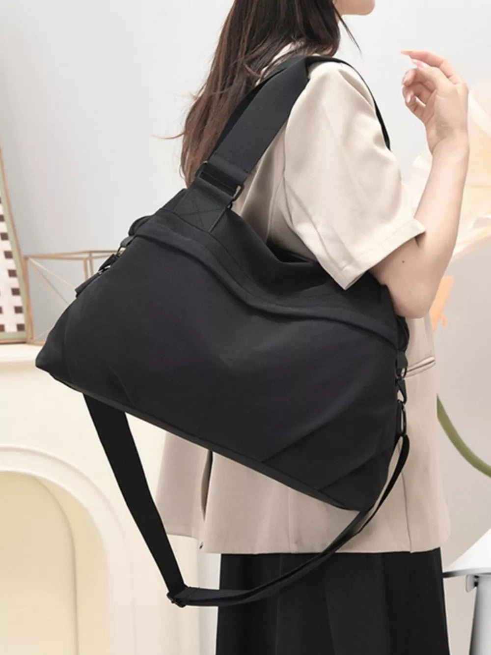 Black nylon duffel bag with adjustable strap and zip closure, worn crossbody.