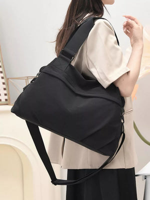 Black nylon duffel bag with adjustable strap and zip closure, worn crossbody.