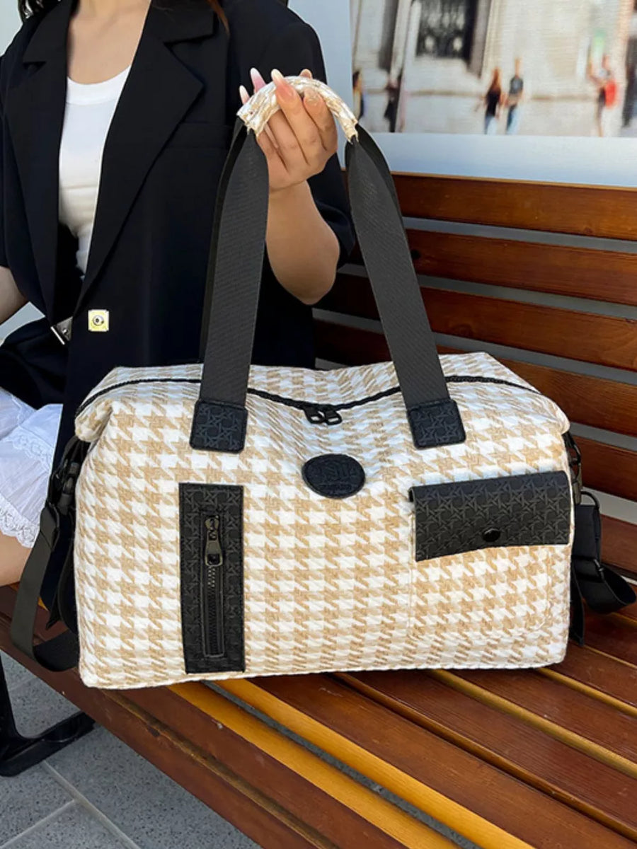 Chic houndstooth duffle bag with black accents and detachable strap.