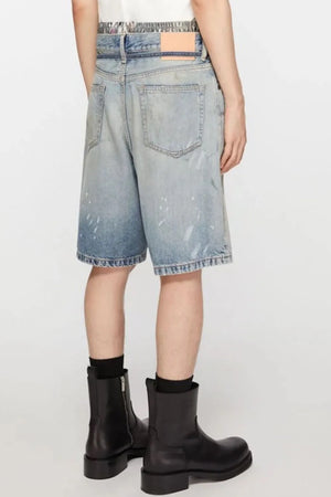 Distressed denim bermuda shorts in medium wash with paint splatters and frayed hem.