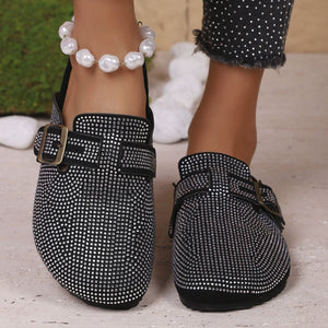 Black rhinestone buckle slip-on mules with adjustable strap and buckle detail.
