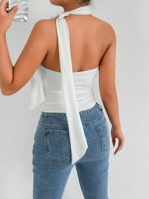 White halter neck top with long tie detail, paired with blue denim jeans.