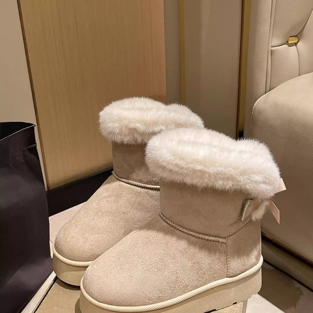 Beige suede round-toe boots with fluffy white trim and a small bow detail.