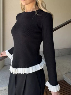 Black ribbed knit sweater with contrast white ruffled trim at hem and cuffs.