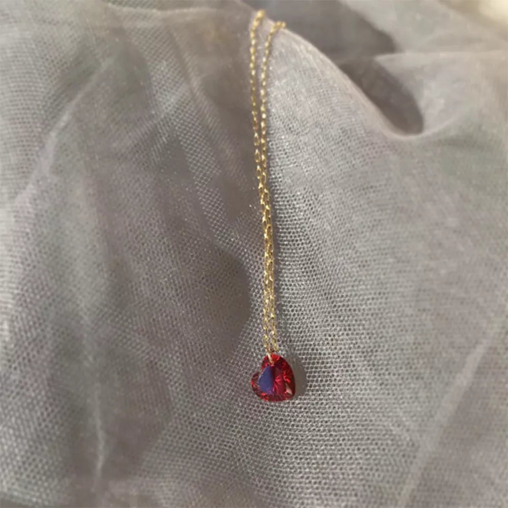 Gold chain necklace with a red heart-shaped zircon pendant.