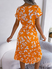Orange midi dress with white leaf print, short sleeves, belted waist, and pleated skirt.