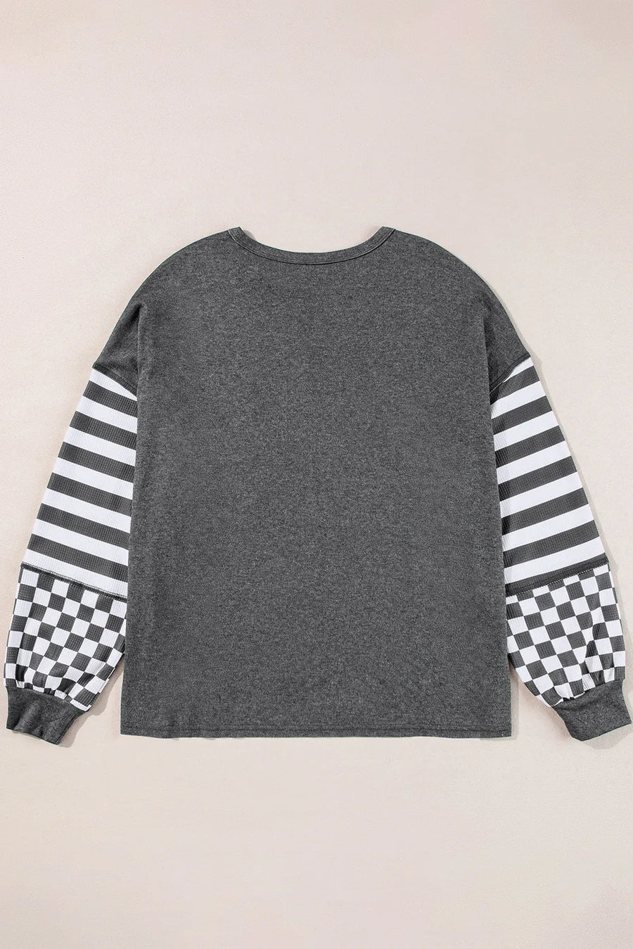 Asymmetrical knit top in charcoal gray with striped and checkered patchwork sleeves.
