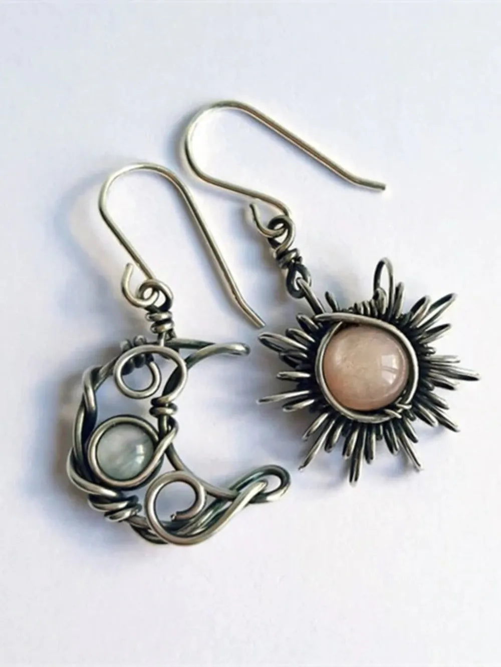 Celestial mismatched drop earrings in silver wirework with moon and sun charms and pink and white stones.