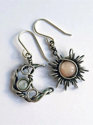 Celestial mismatched drop earrings in silver wirework with moon and sun charms and pink and white stones.