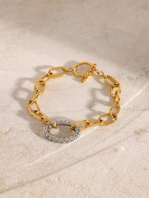 Gold chain toggle bracelet with a textured silver ring detail.