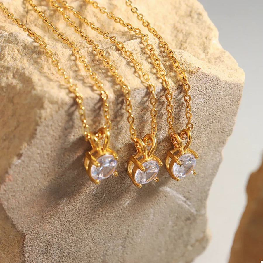 Gold zircon pendant necklaces with delicate chains displayed on a textured surface.