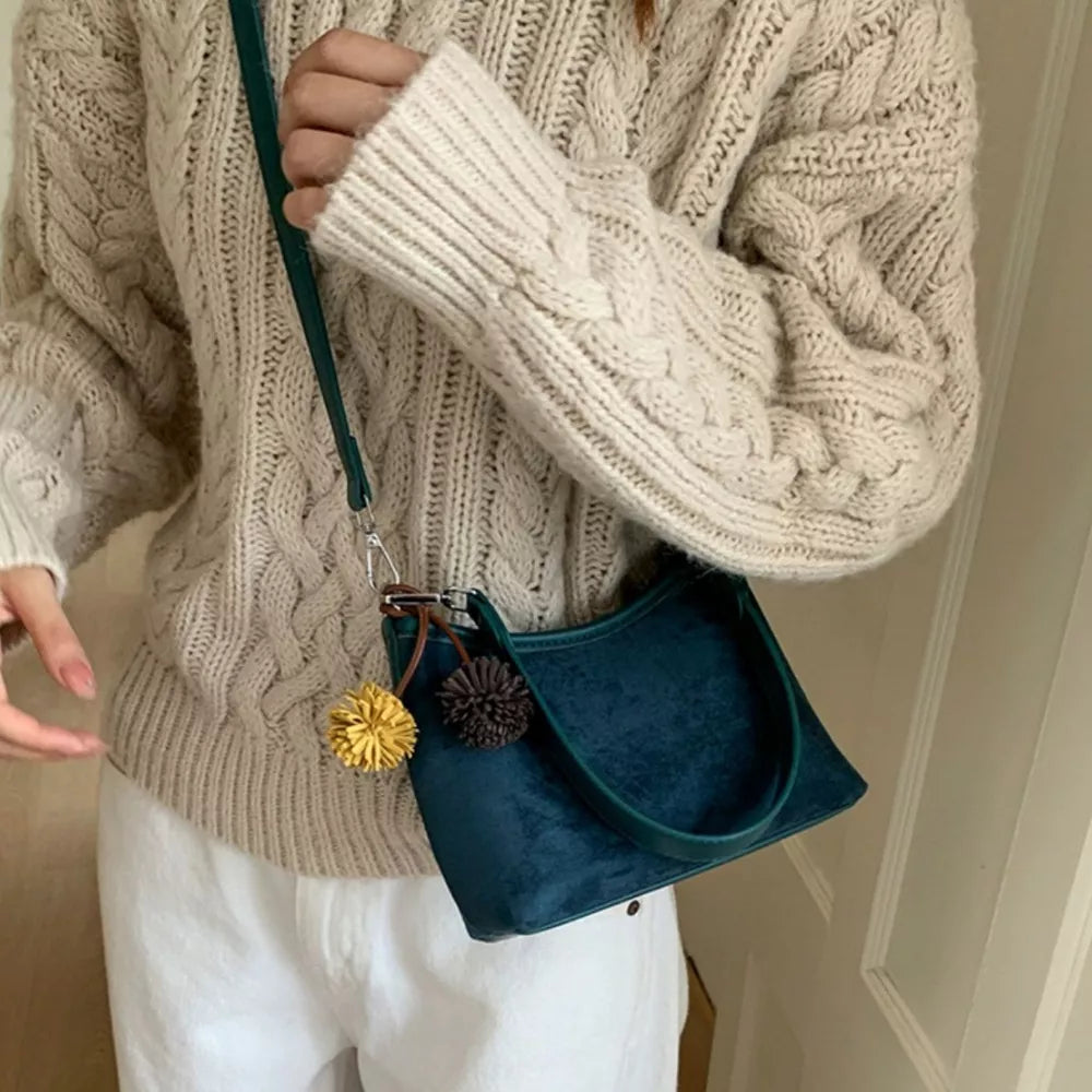 Blue suede crossbody bag with yellow and brown pom-pom charms and adjustable strap.