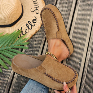 Brown suede slip-on flats with decorative stitching and a gold chain detail.