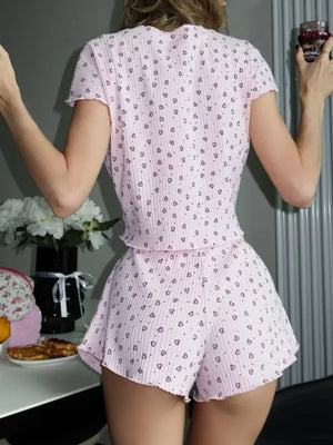 Pink ribbed pajama set with allover heart print, featuring a short sleeve top and ruffled hem shorts.