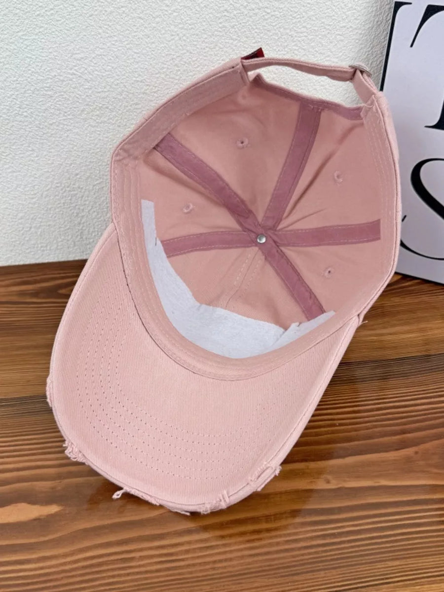 Pink distressed baseball cap with adjustable strap and embroidered detail.