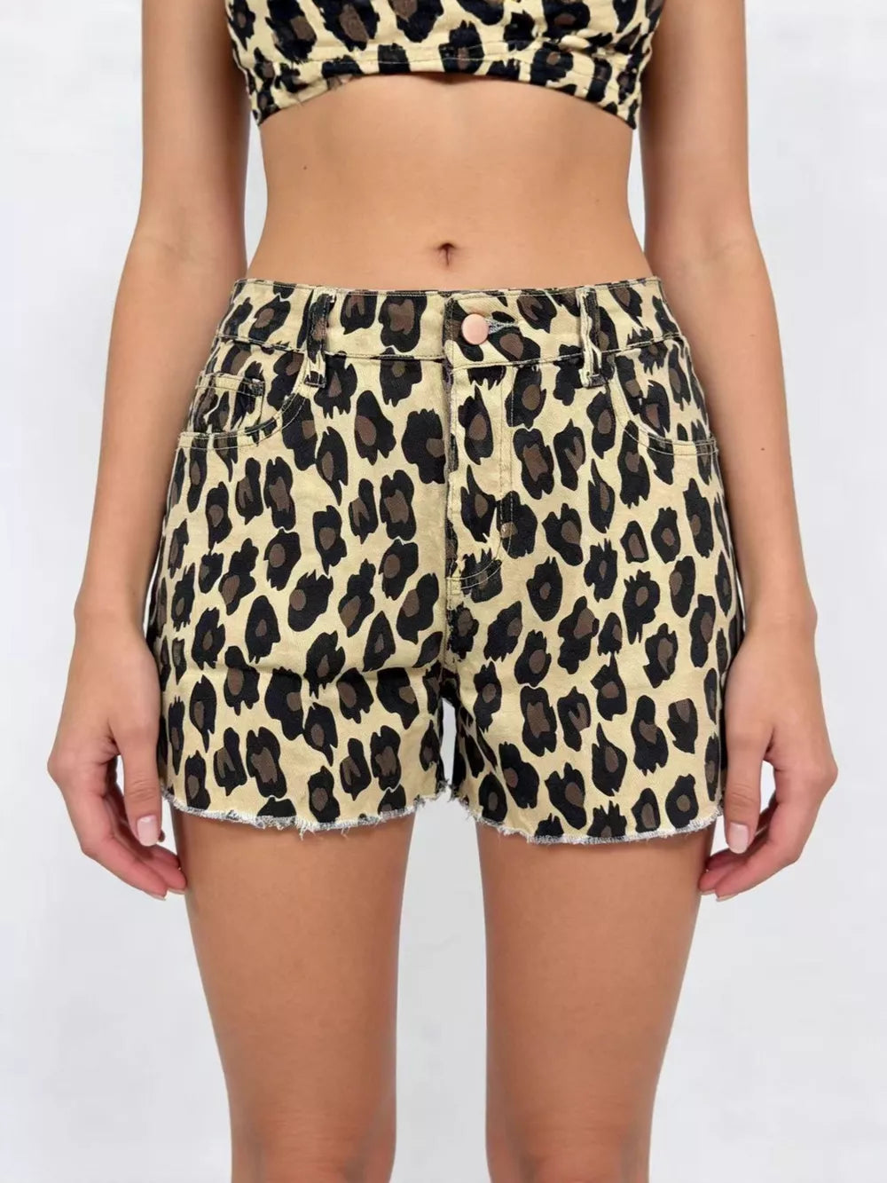 Leopard print high-waisted denim shorts with raw hem and button fly.