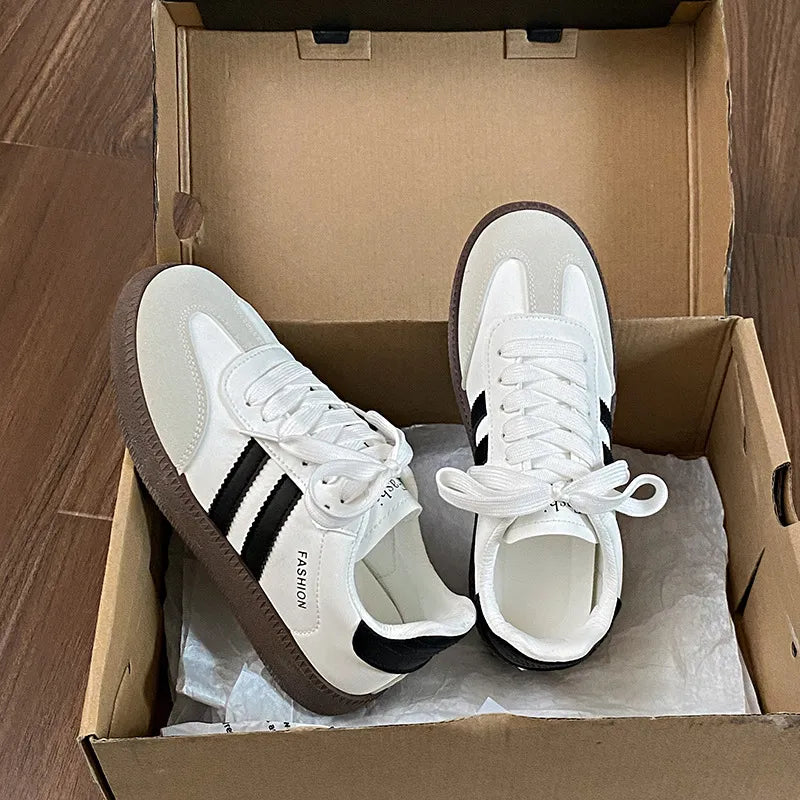 White leather sneakers with black stripes and branding, brown soles, lace-up closure.