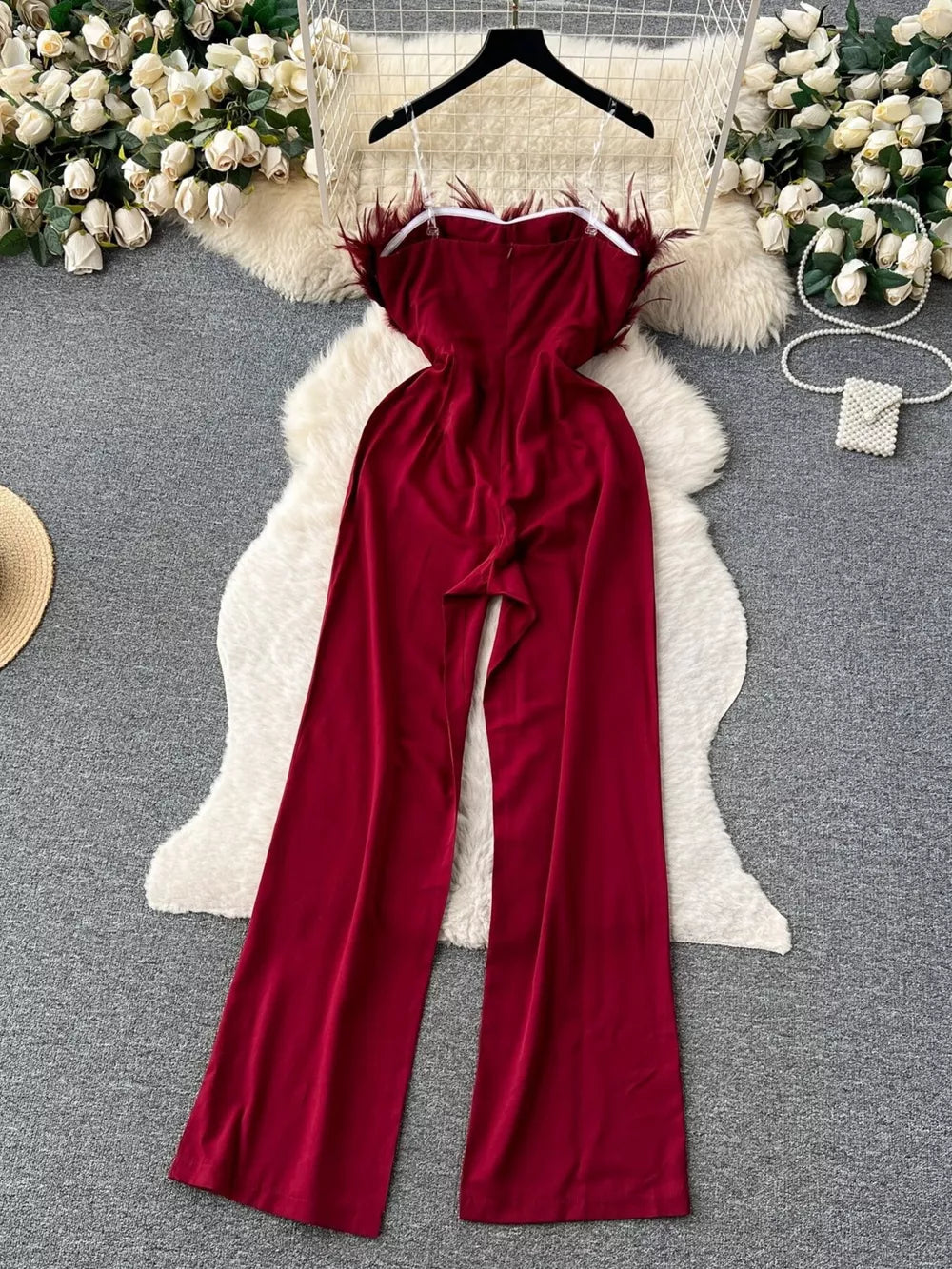 Wine red strapless wide-leg jumpsuit with feather trim and a belted waist.