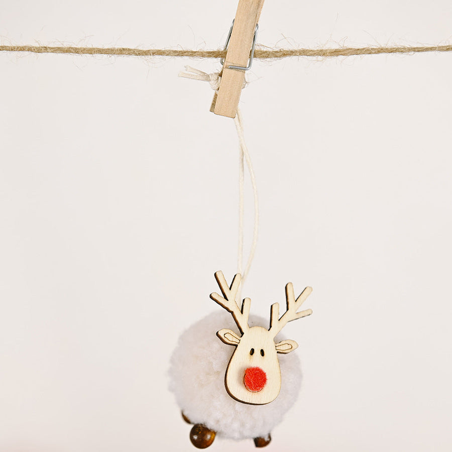 Whimsical pom-pom reindeer ornament with wooden antlers and red nose, hanging on twine.