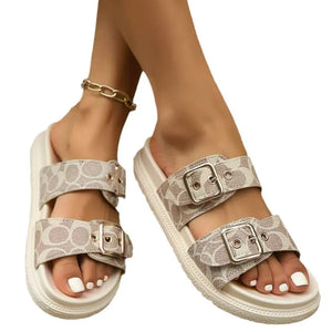 Beige logo slide sandals with double buckle straps and white toenails.