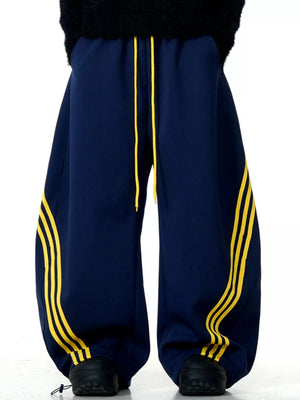 Men's navy blue wide-leg sweatpants with yellow side stripes and drawstring waist.