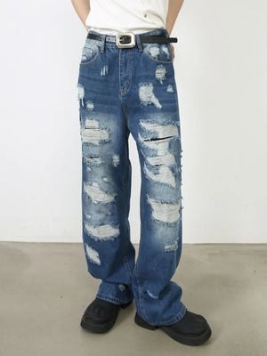 Oversized ripped denim jeans in medium wash with raw edge details and distressed accents.