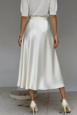 White a-line midi skirt with a lustrous finish and hidden pockets, styled with a white top and heels.