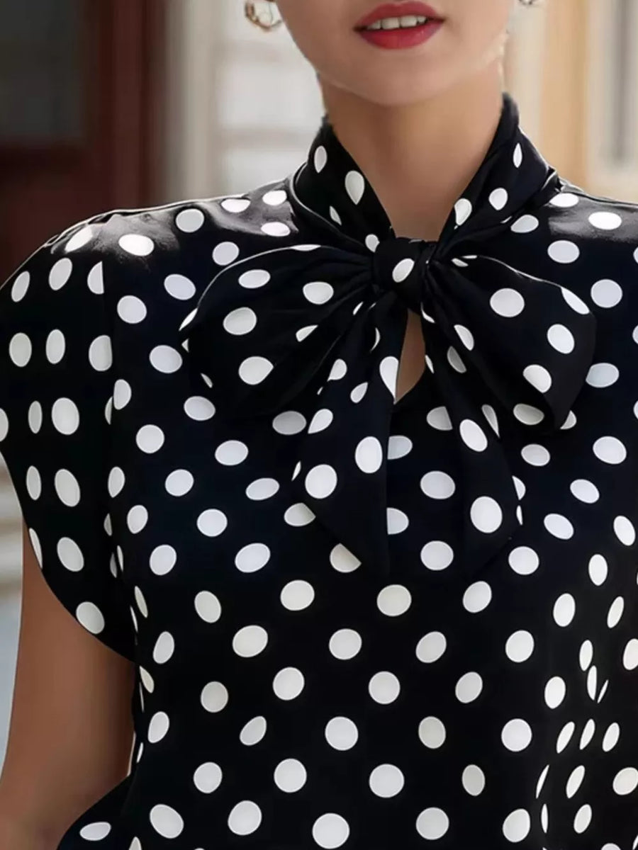 Black and white polka dot shirt with a bow tie neck and cap sleeves.