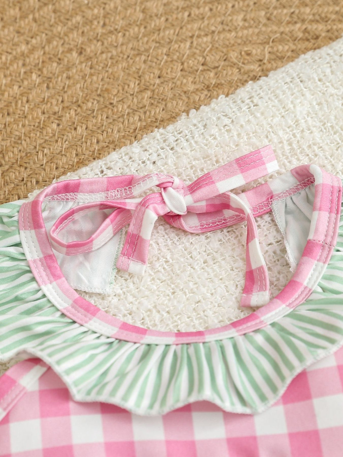 Baby one-piece swimsuit with pink gingham and green stripes, featuring ruffle trim and tie straps.