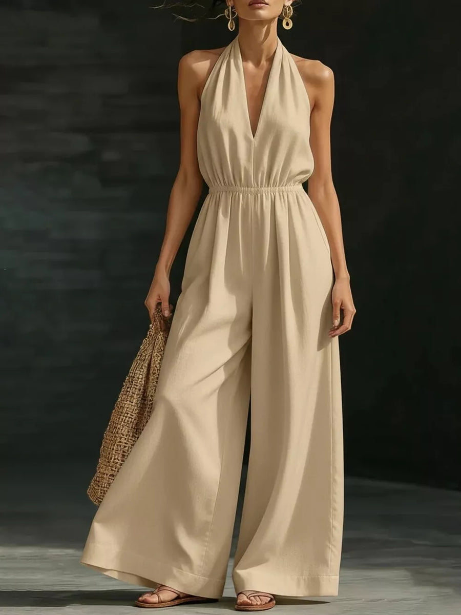Apricot halter jumpsuit with wide legs and elastic waist, styled with sandals and a straw bag.